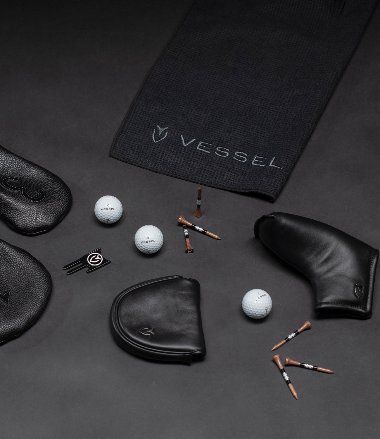 Black leather golf headcovers, a black magnetic golf towel, golf tees, golf balls, and a divot tool on a black background.