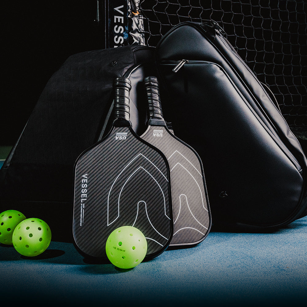 Carbon pickleball paddles leaned against leather pickleball paddle bags with 3 pickleballs on the ground