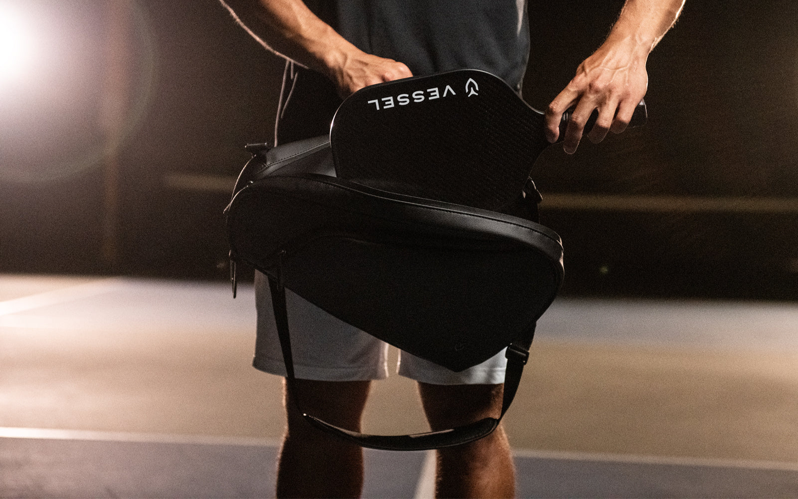 Black carbon pickleball paddle being put into black leather pickleball bag on pickleball court
