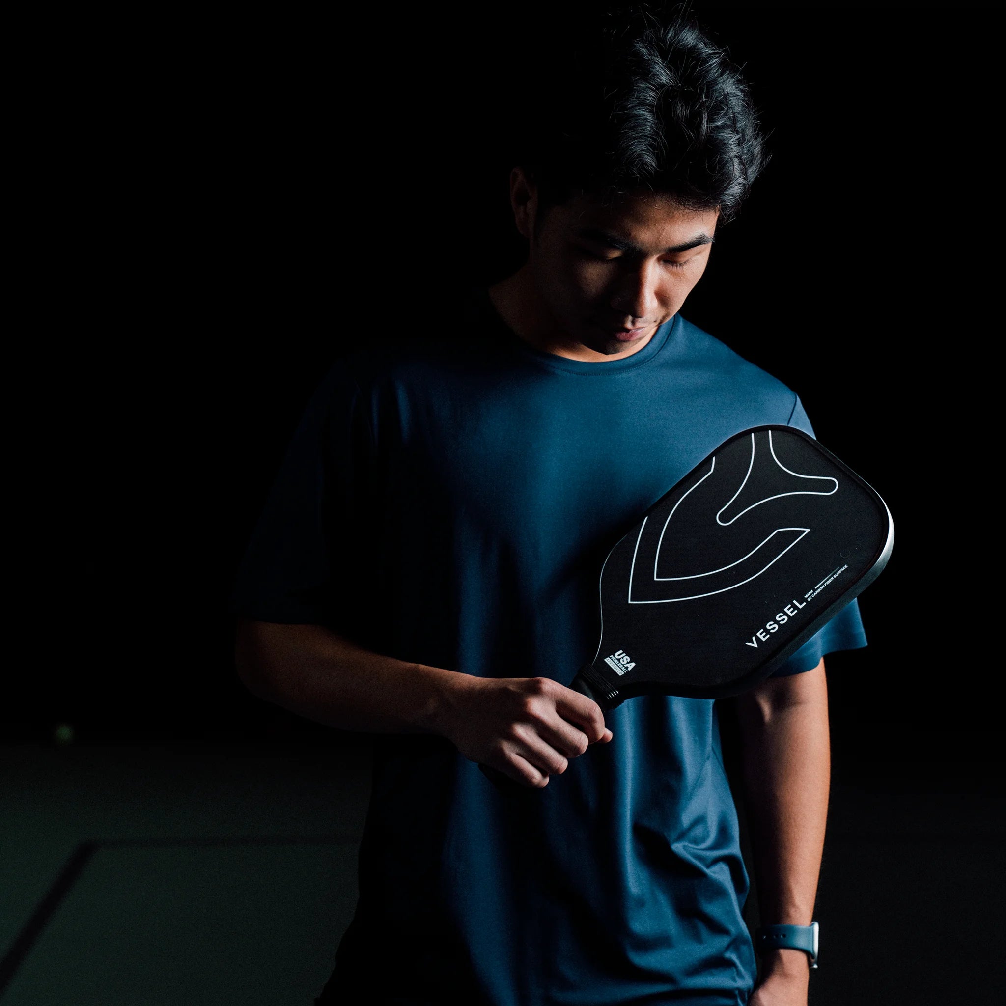 Man holding Black carbon fiber pickleball paddle with Vessel branding on the face in dramatic lighting