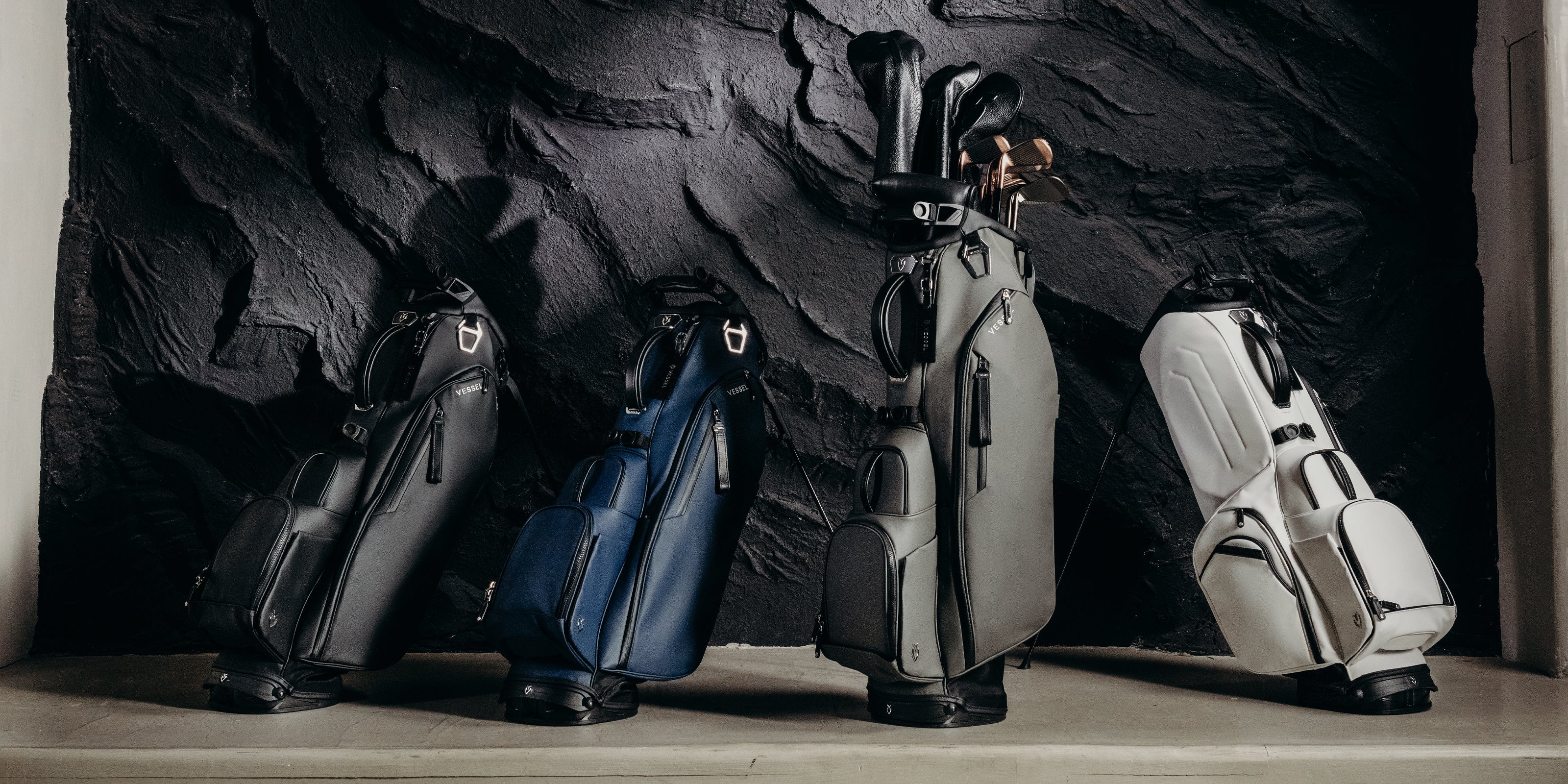 Four Player V stand bags lined up against a black stone wall