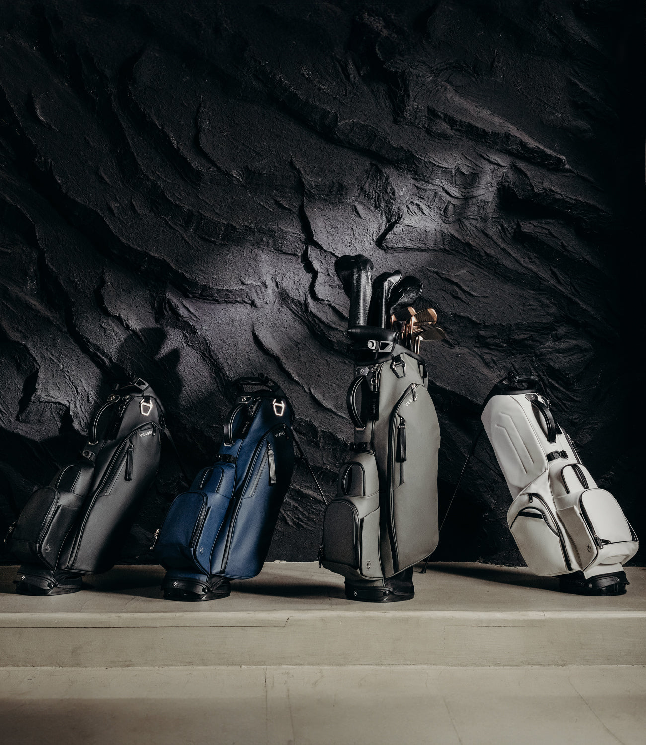Four Player V stand bags lined up against a black stone wall