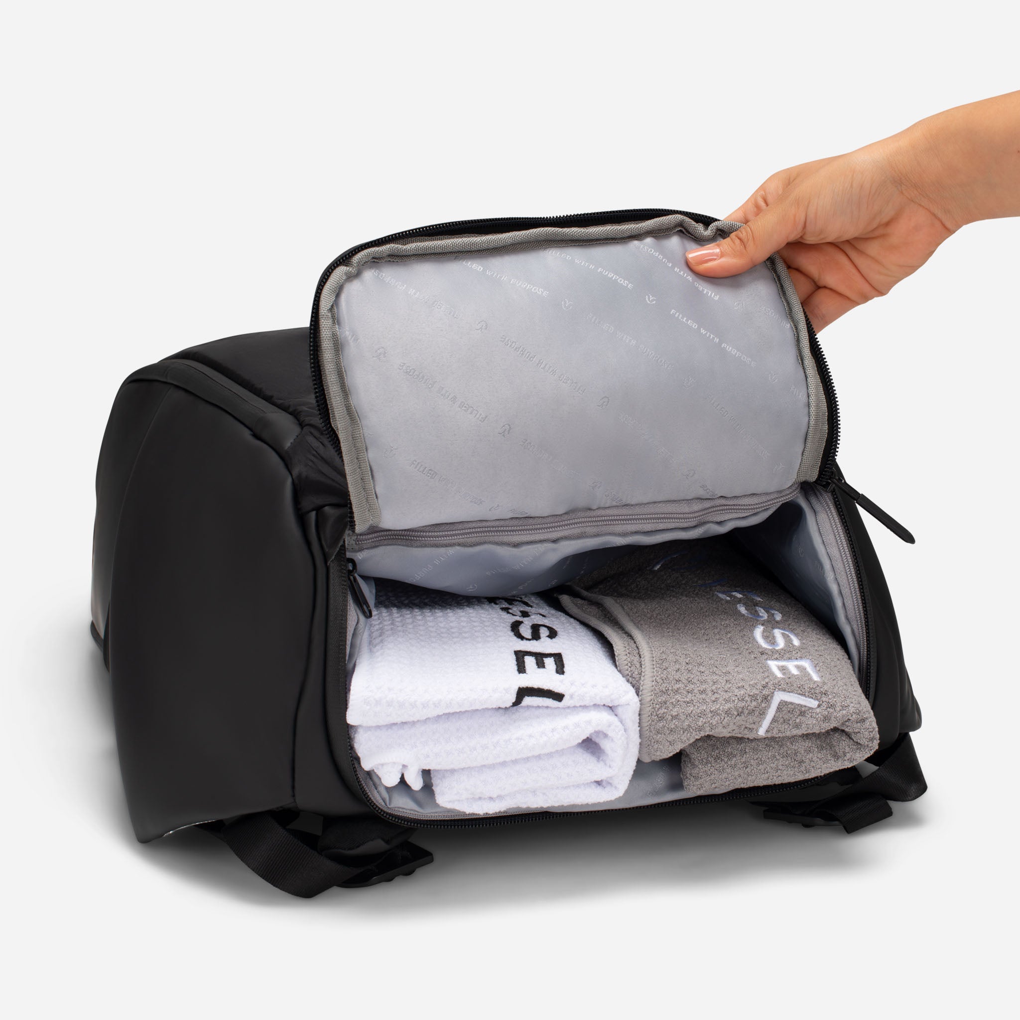 Open bottom of black tennis back pack with folded white and grey towels inside