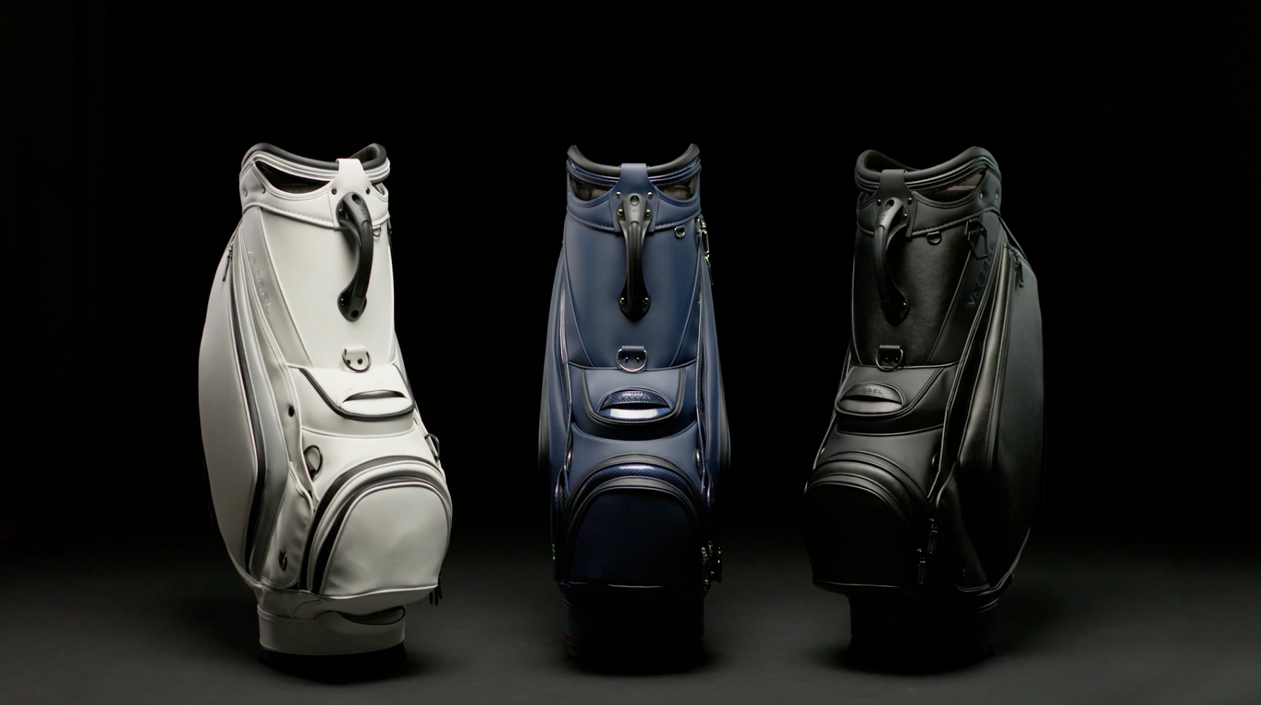 Three Prime 2.0 golf staff bags, one white, one blue, and one black, next to each other in a black studio