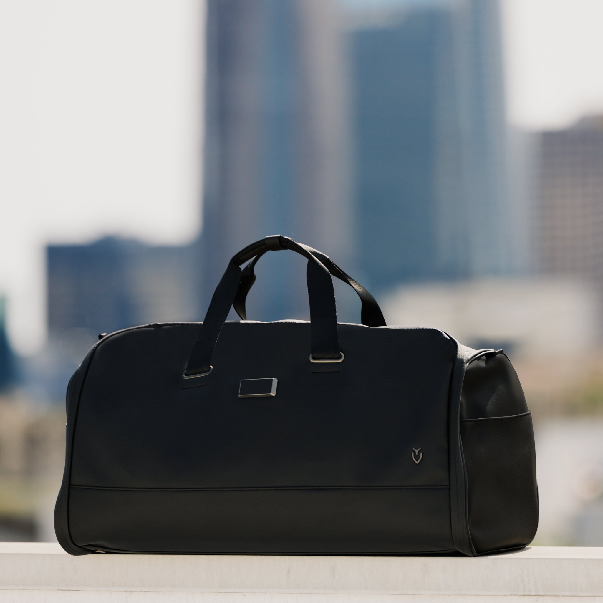 Black garment duffel bag with a cityscape behind it  #color_pebbled black