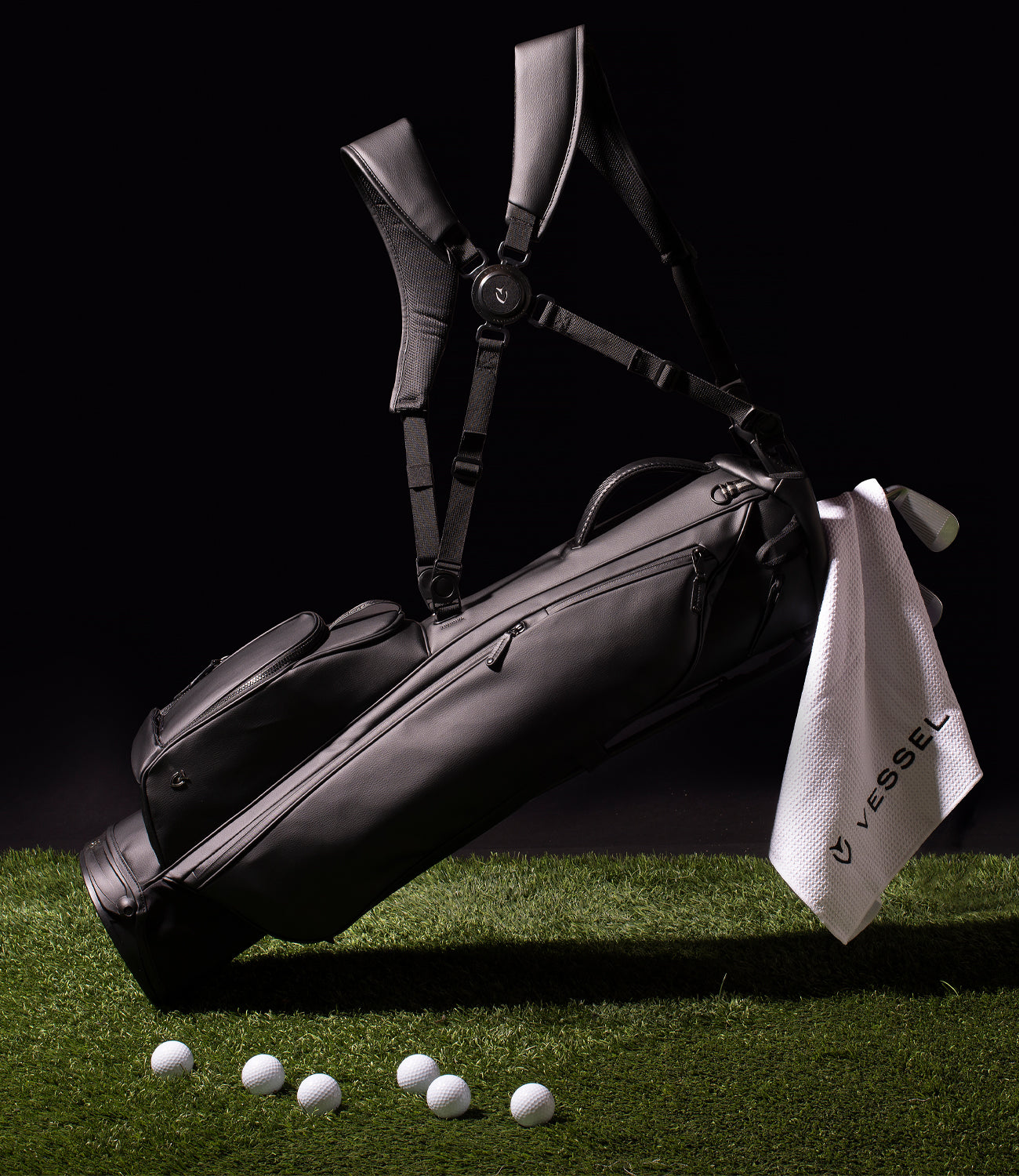 Black floating golf stand bag with hanging white towel on green grass with scattered golf balls