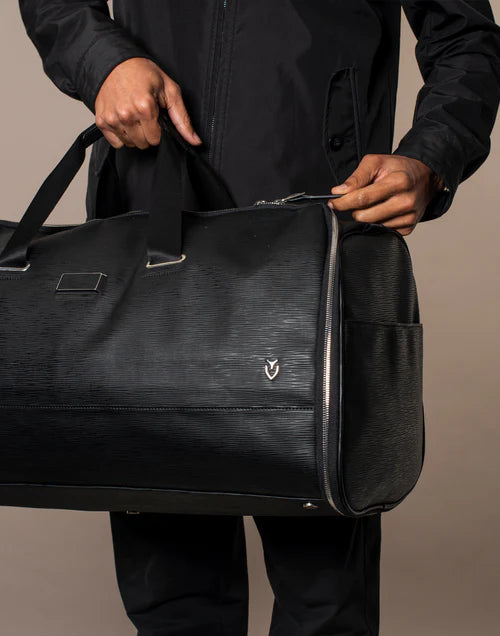 Model wearing all black carries a black leather backpack in a brown studio