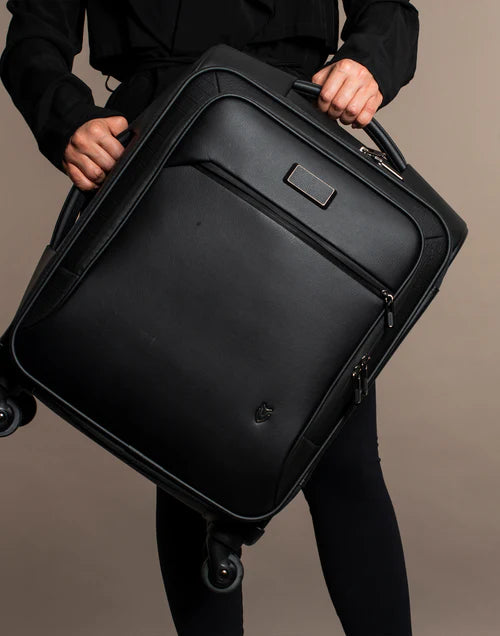 Model wearing black holds a black Signature Luggage in a brown studio