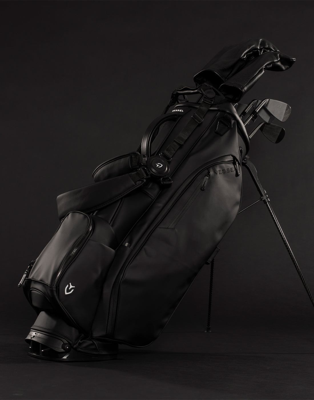 Black golf stand bag filled with golf clubs propped up in black studio