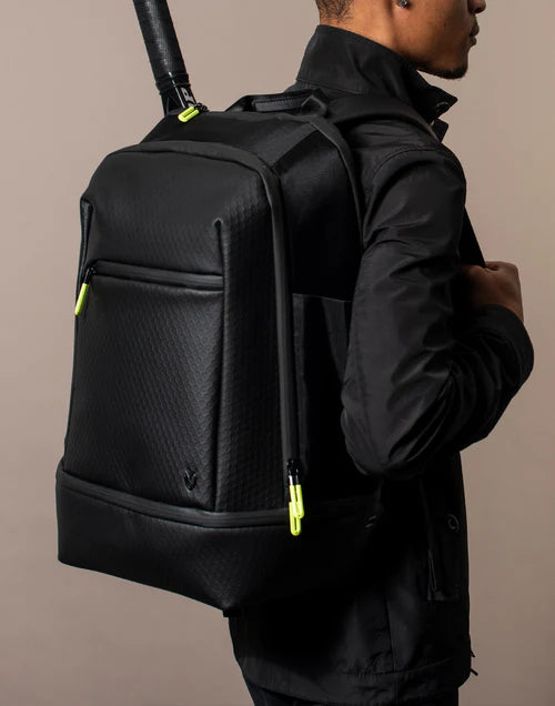 Man wearing all black carries the black Baseline Tennis Backpack on his back in a brown studio