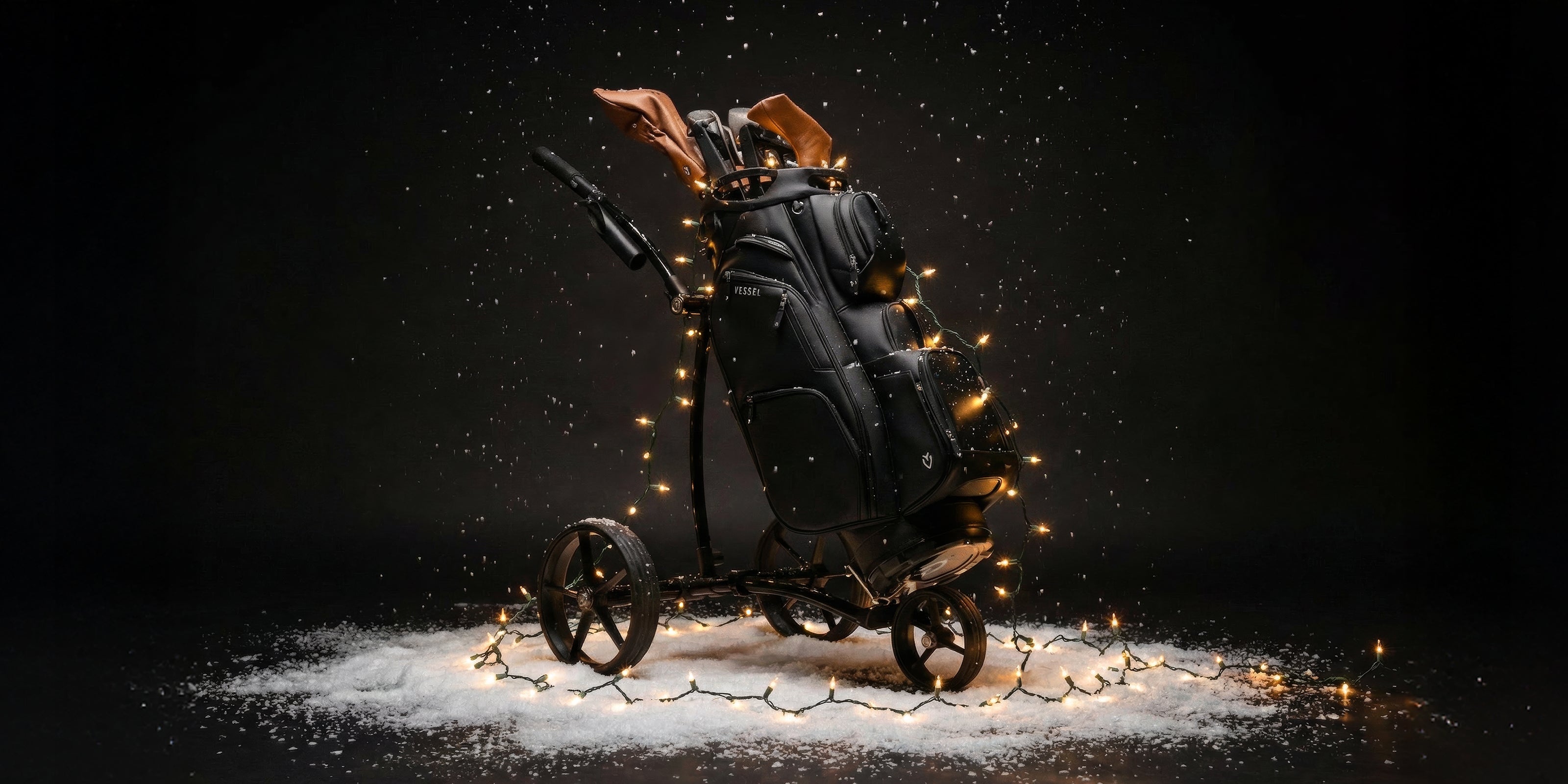 Black cart bag on push cart covered in Christmas lights on snowy background
