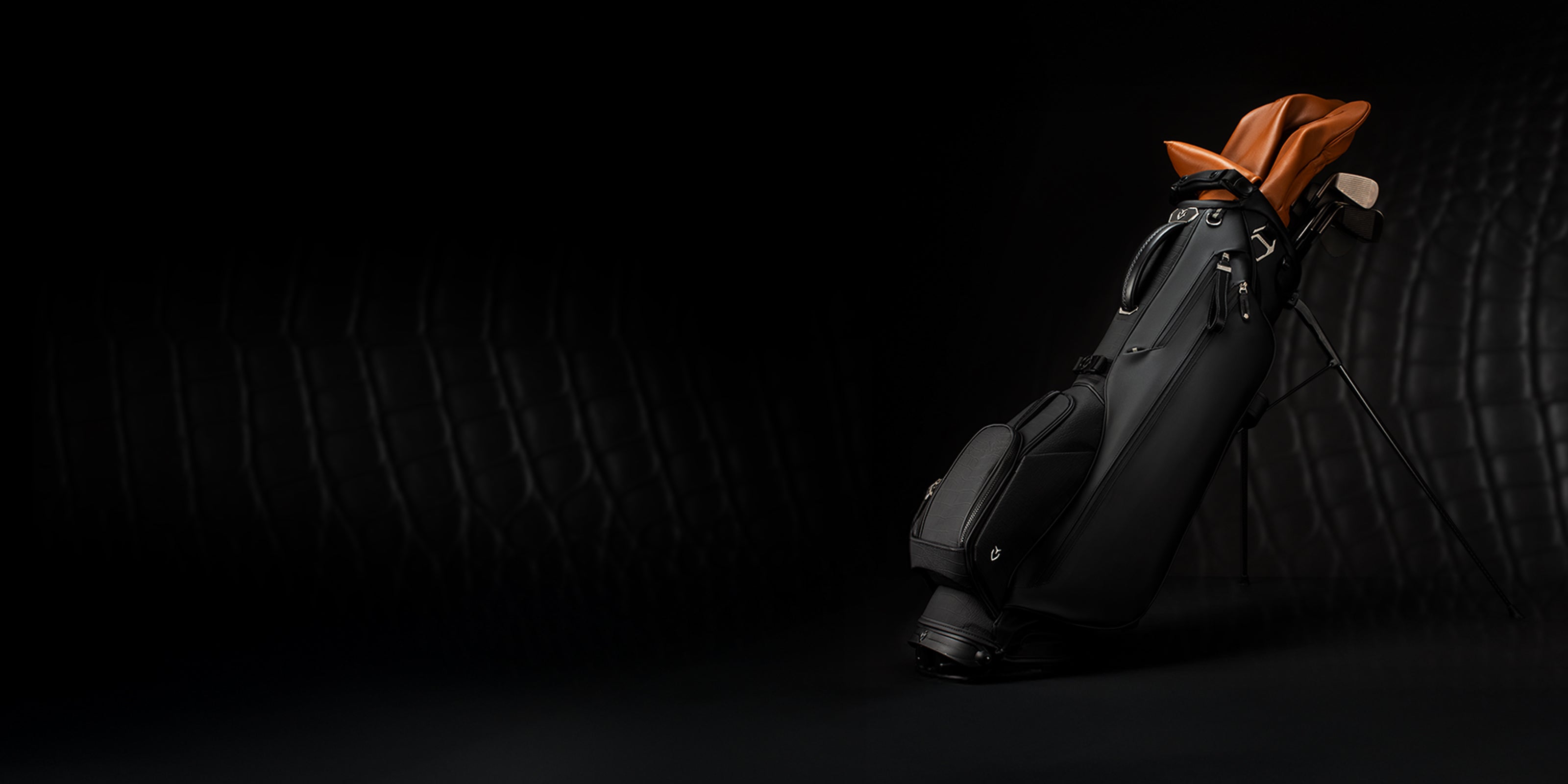 Croc Black Lux Stand golf bag on black background. Bag contains clubs with brown headcovers