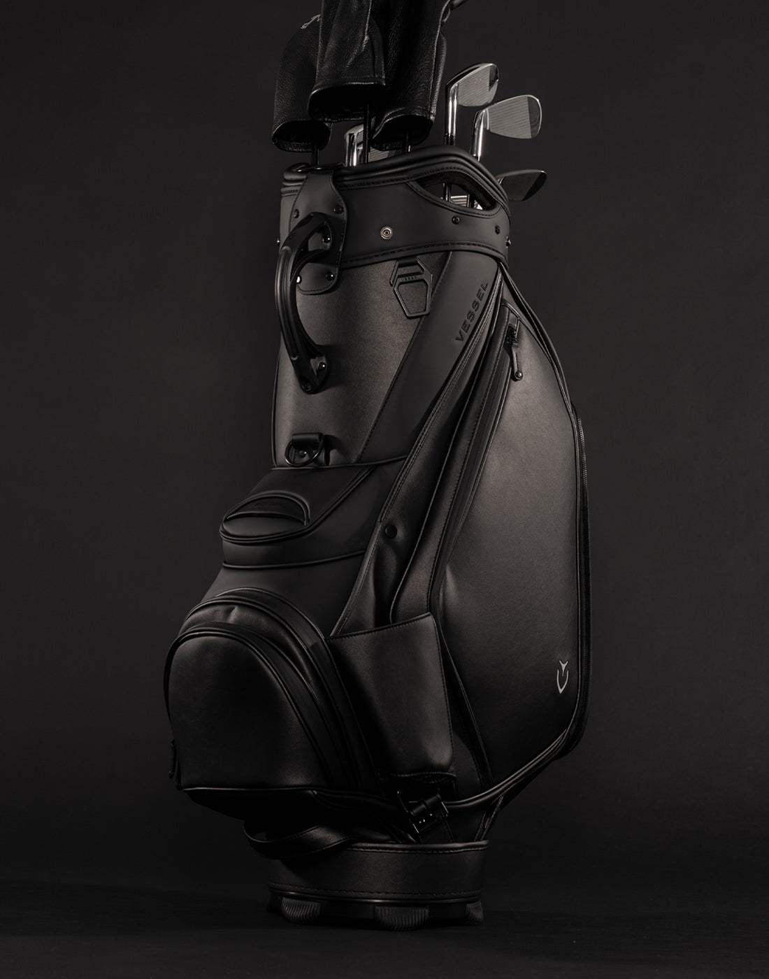 Black golf staff bag filled with golf clubs propped upright in black studio