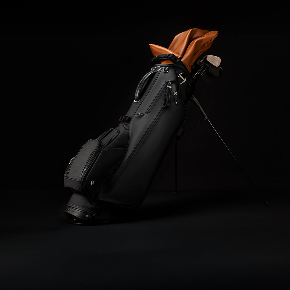 Croc Black Lux Stand golf bag on black background. Bag contains clubs with brown headcovers